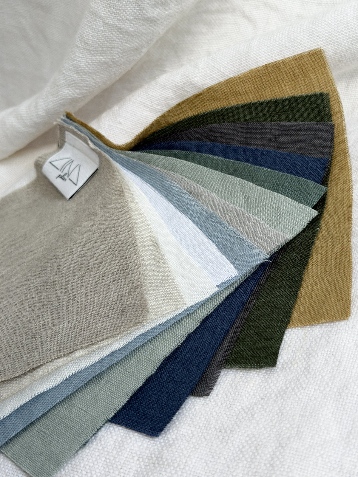Linen Samples MIDILINO fanned fabric swatches in earth, blue, and neutral tones with tag